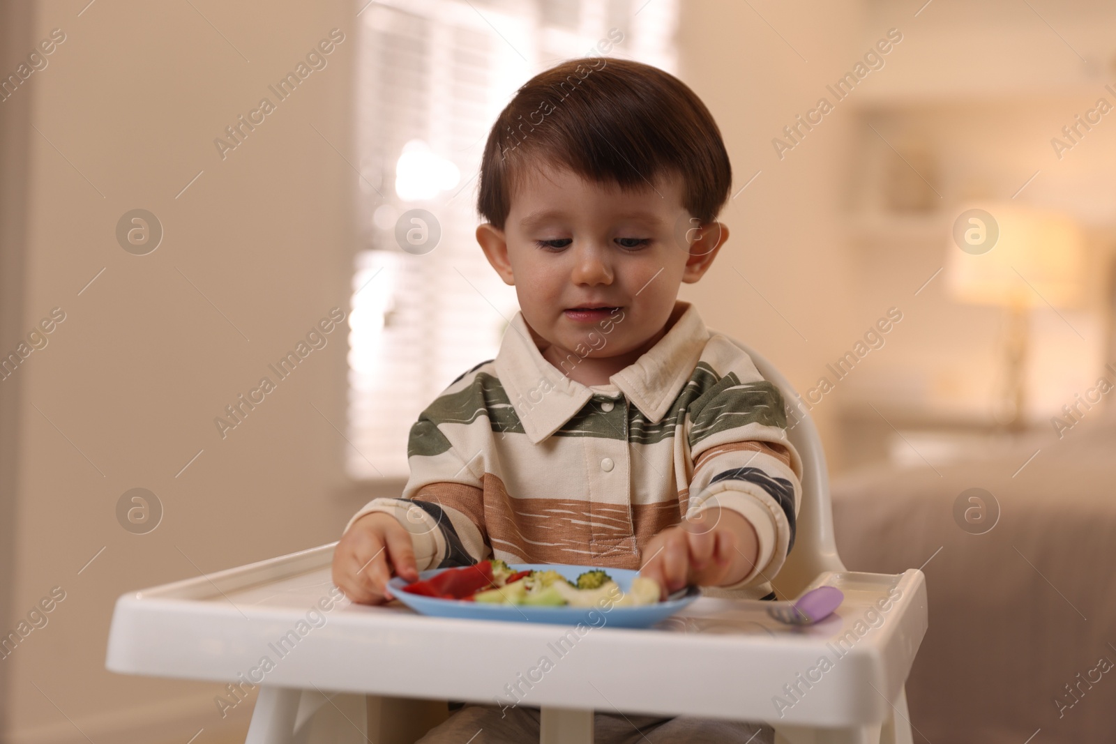 Photo of Cute little baby eating healthy food in high chair at home