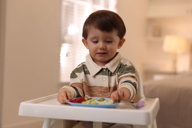 Cute little baby eating healthy food in high chair at home