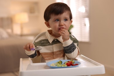 Cute little baby eating healthy food in high chair at home