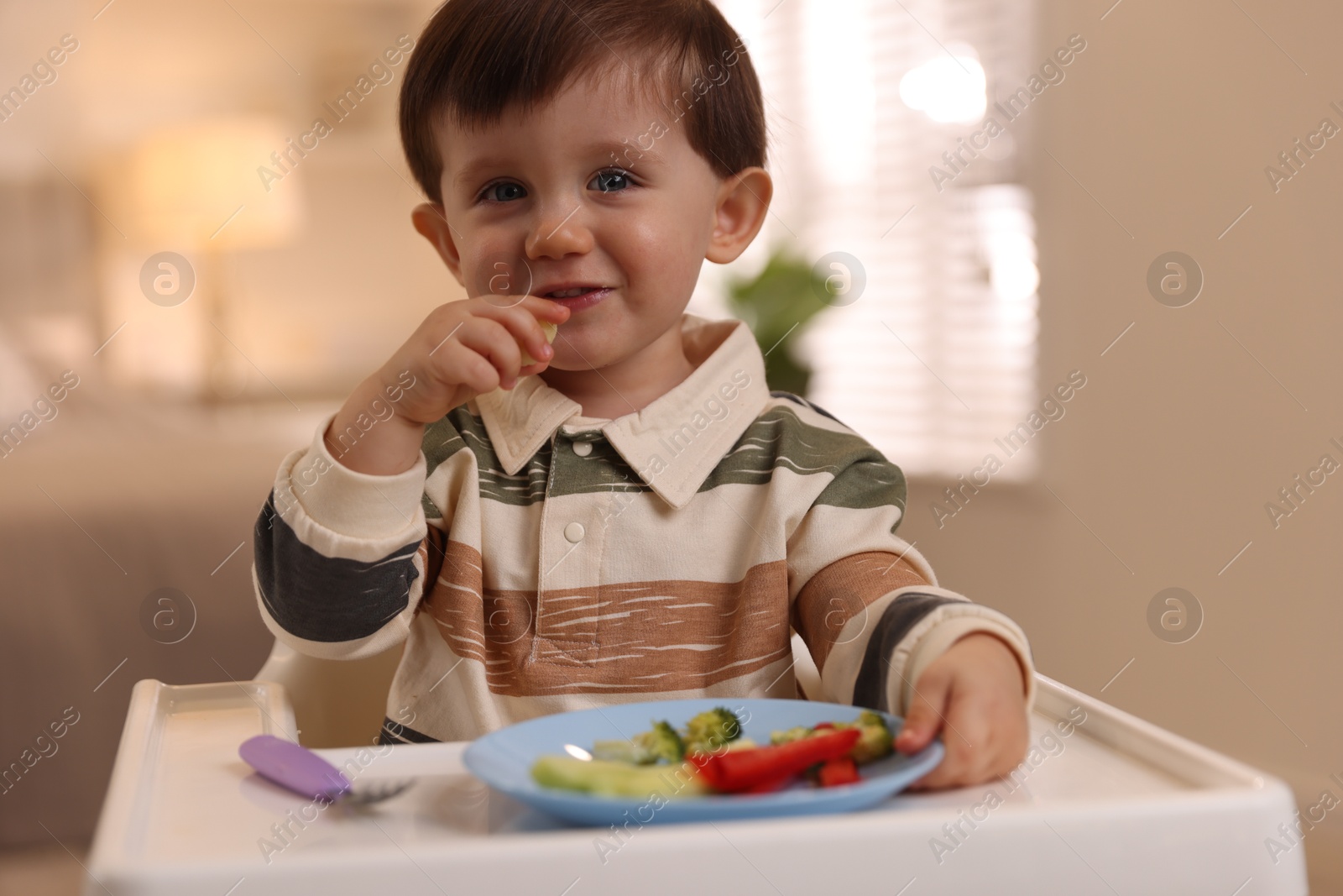 Photo of Cute little baby eating healthy food in high chair at home