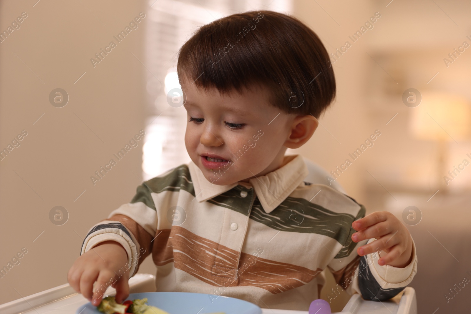 Photo of Cute little baby eating healthy food in high chair at home