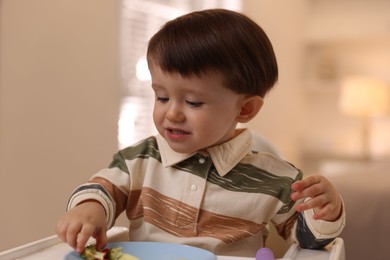 Cute little baby eating healthy food in high chair at home