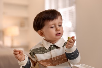 Cute little baby eating healthy food in high chair at home