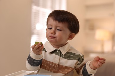 Photo of Cute little baby eating healthy food in high chair at home