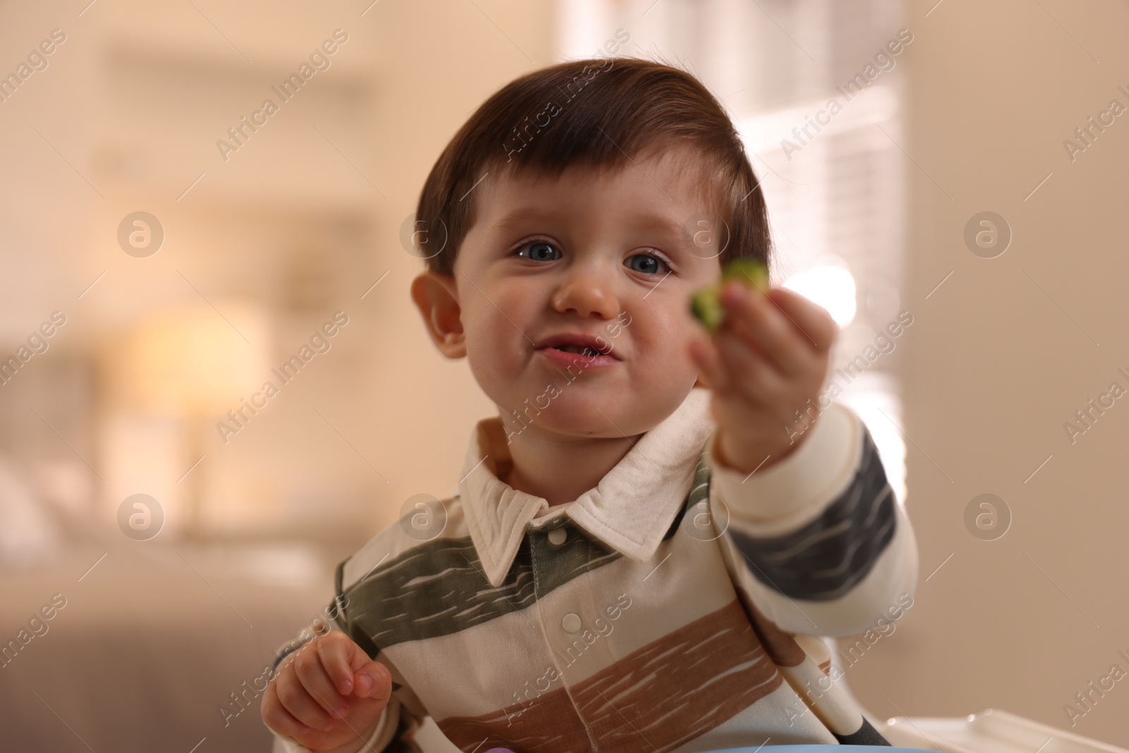 Photo of Cute little baby eating healthy food in high chair at home