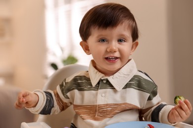 Photo of Cute little baby eating healthy food in high chair at home