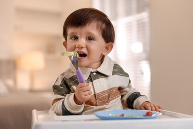 Photo of Cute little baby eating healthy food in high chair at home