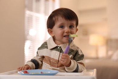 Photo of Cute little baby eating healthy food in high chair at home