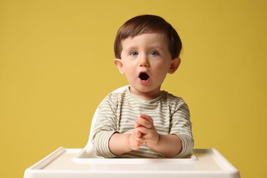 Photo of Cute little kid sitting in high chair on yellow background