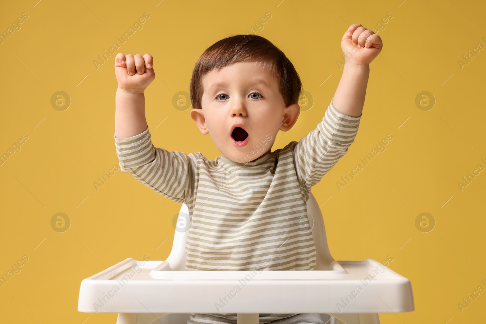 Photo of Cute little kid sitting in high chair on yellow background