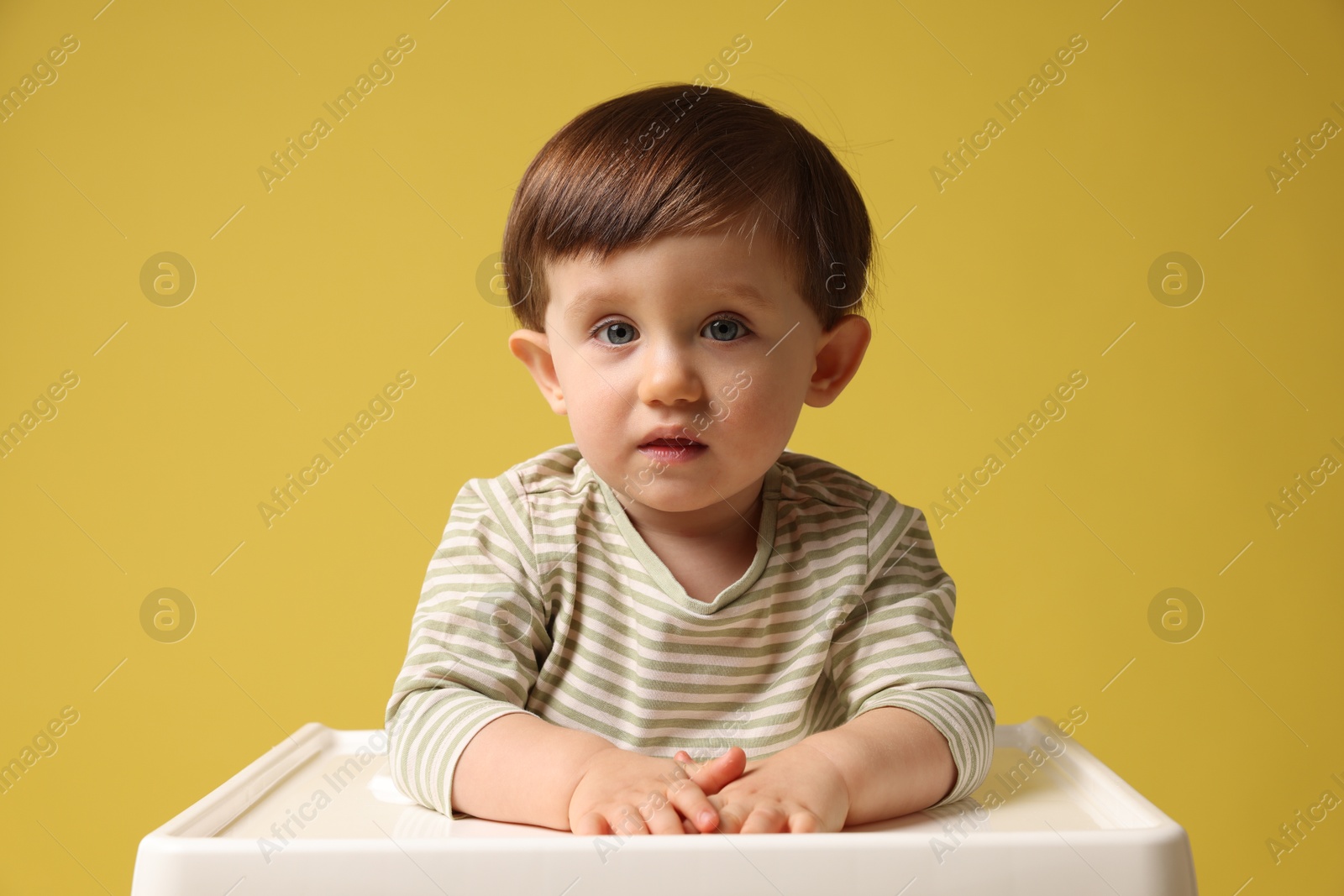 Photo of Cute little kid sitting in high chair on yellow background