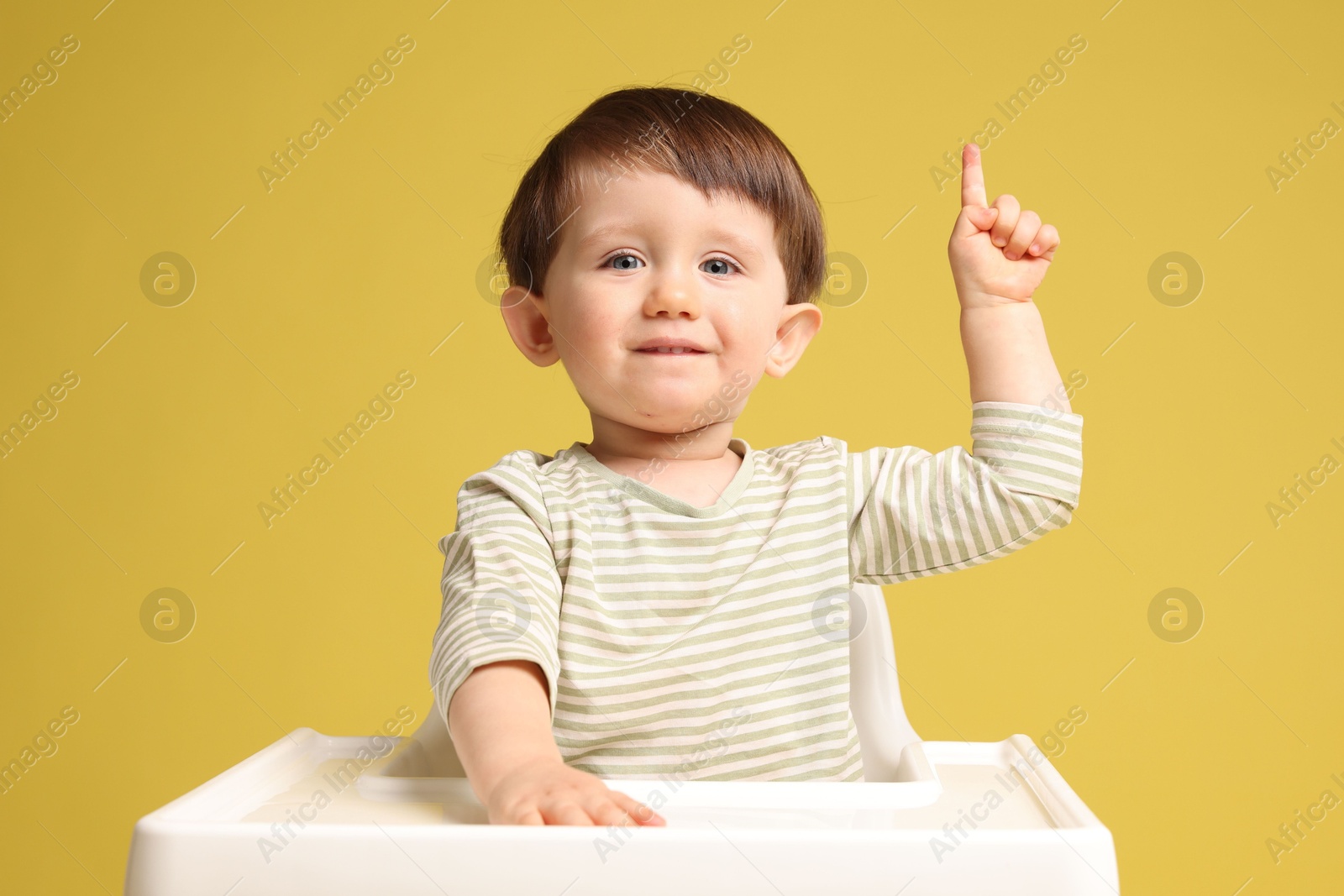 Photo of Cute little kid sitting in high chair on yellow background