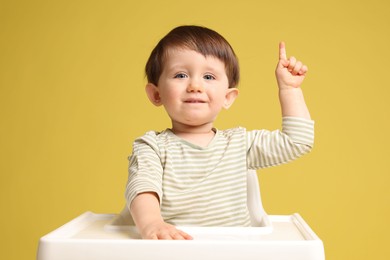 Cute little kid sitting in high chair on yellow background