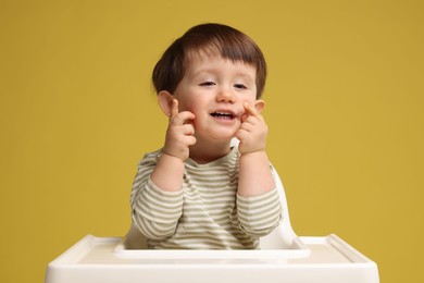 Photo of Cute little kid sitting in high chair on yellow background