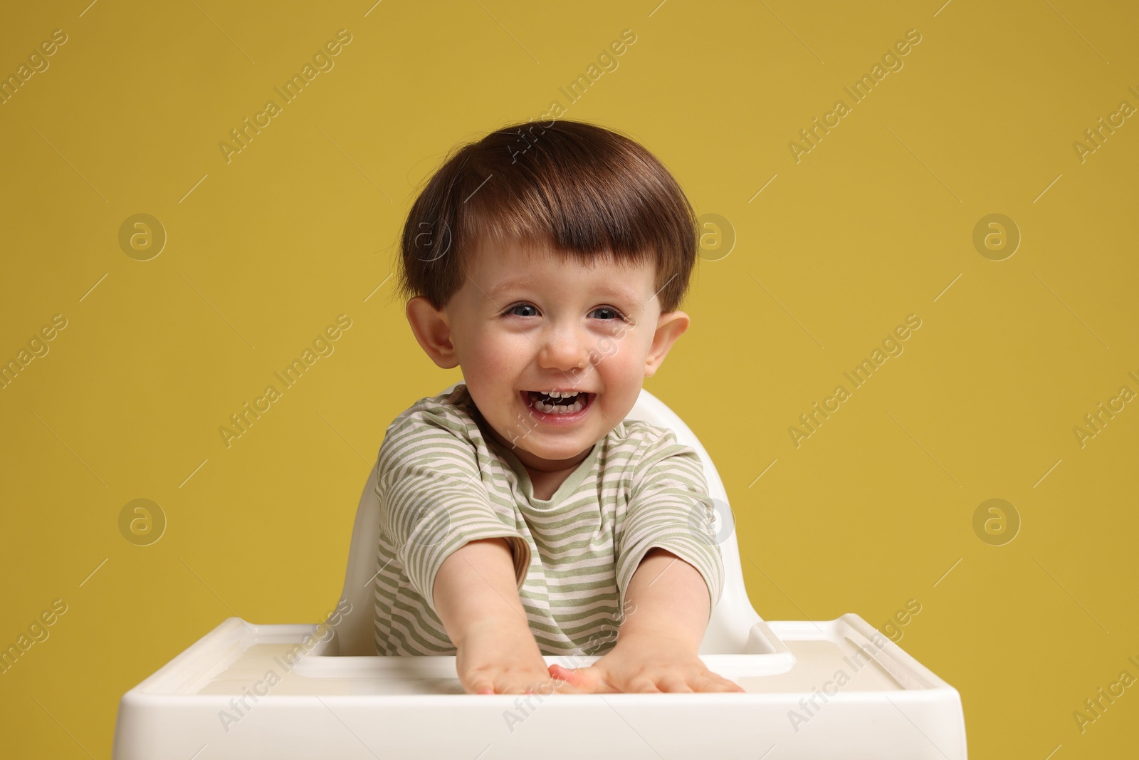 Photo of Cute little kid sitting in high chair on yellow background