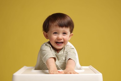 Photo of Cute little kid sitting in high chair on yellow background