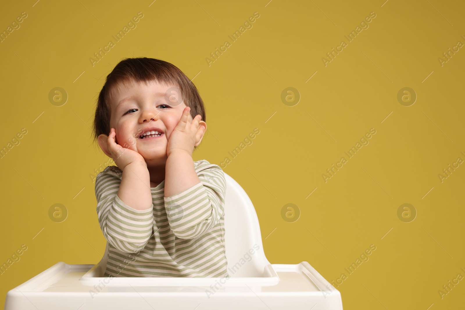 Photo of Cute little kid sitting in high chair on yellow background, space for text