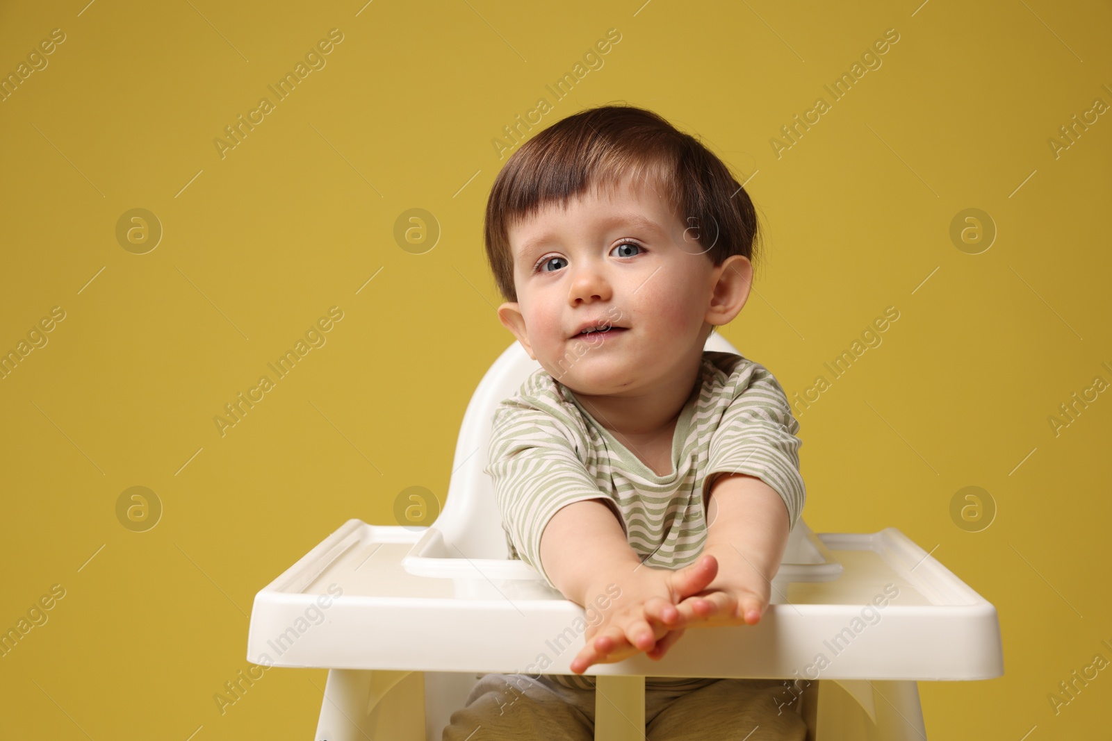 Photo of Cute little kid sitting in high chair on yellow background