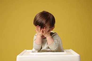 Photo of Cute little kid sitting in high chair on yellow background