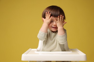 Photo of Cute little kid sitting in high chair on yellow background