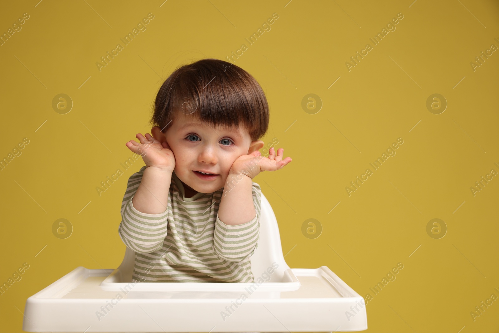 Photo of Cute little kid sitting in high chair on yellow background, space for text