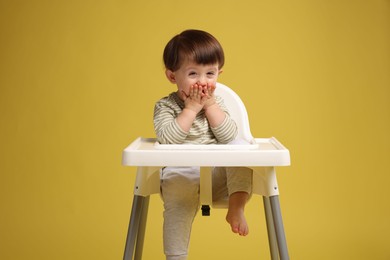 Photo of Cute little kid sitting in high chair on yellow background