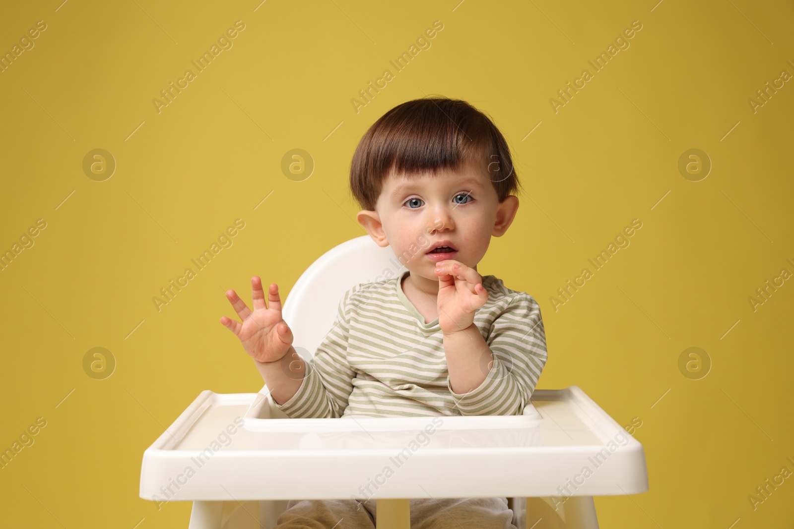 Photo of Cute little kid sitting in high chair on yellow background