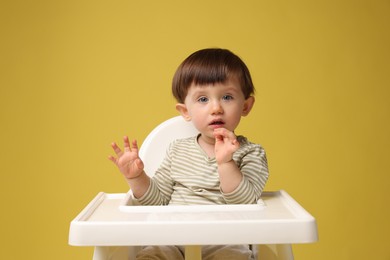 Cute little kid sitting in high chair on yellow background