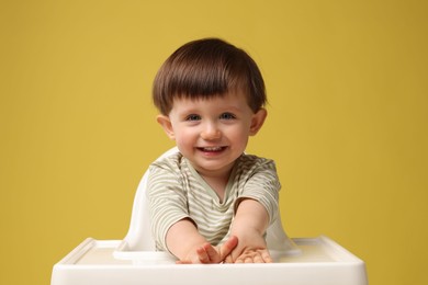 Cute little kid sitting in high chair on yellow background