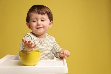 Photo of Cute little kid eating healthy baby food from bowl in high chair on yellow background, space for text