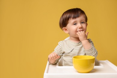 Photo of Cute little kid eating healthy baby food from bowl in high chair on yellow background, space for text