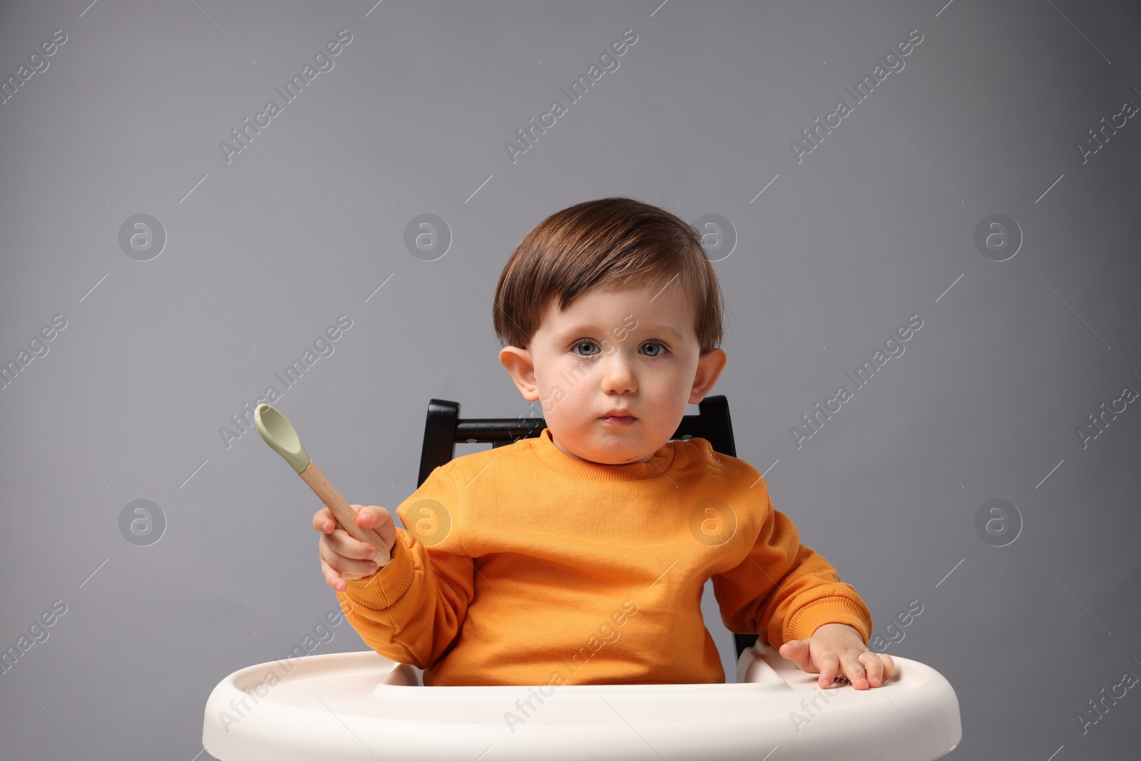 Photo of Cute little kid with spoon sitting in high chair on light grey background