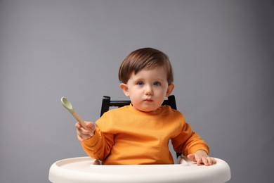 Photo of Cute little kid with spoon sitting in high chair on light grey background