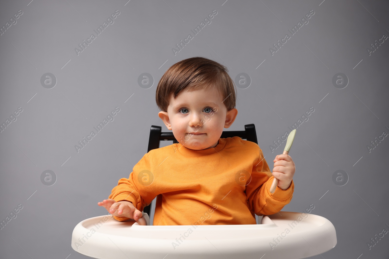 Photo of Cute little kid with spoon sitting in high chair on light grey background