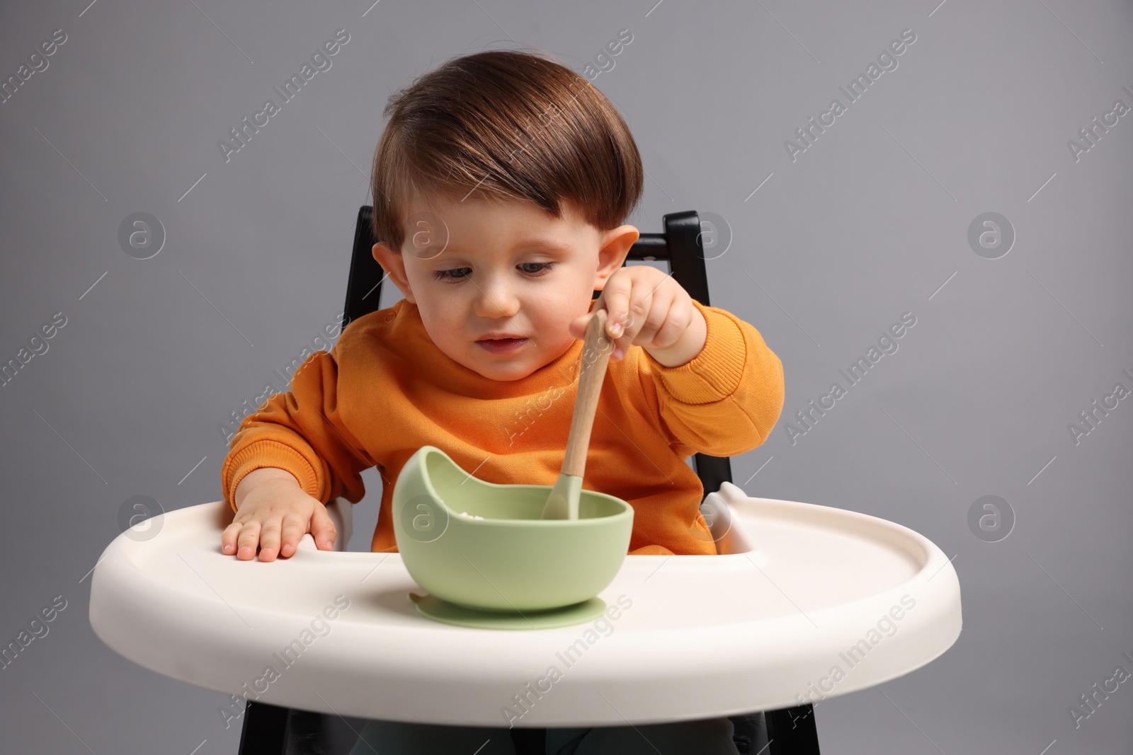 Photo of Cute little kid eating healthy baby food from bowl in high chair on light grey background