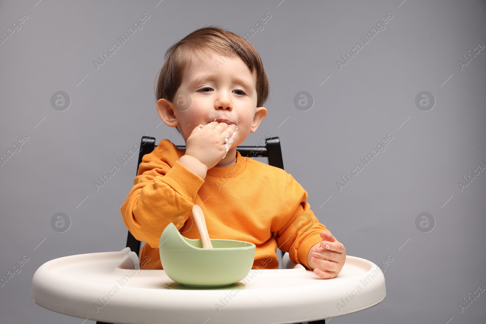 Photo of Cute little kid eating healthy baby food from bowl in high chair on light grey background