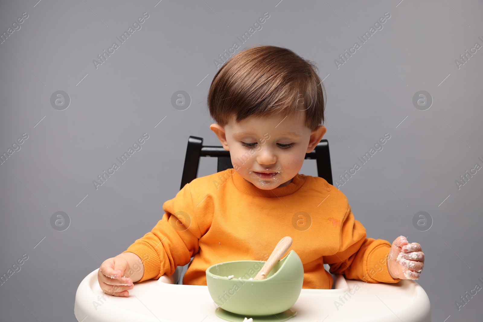 Photo of Cute little kid eating healthy baby food from bowl in high chair on light grey background