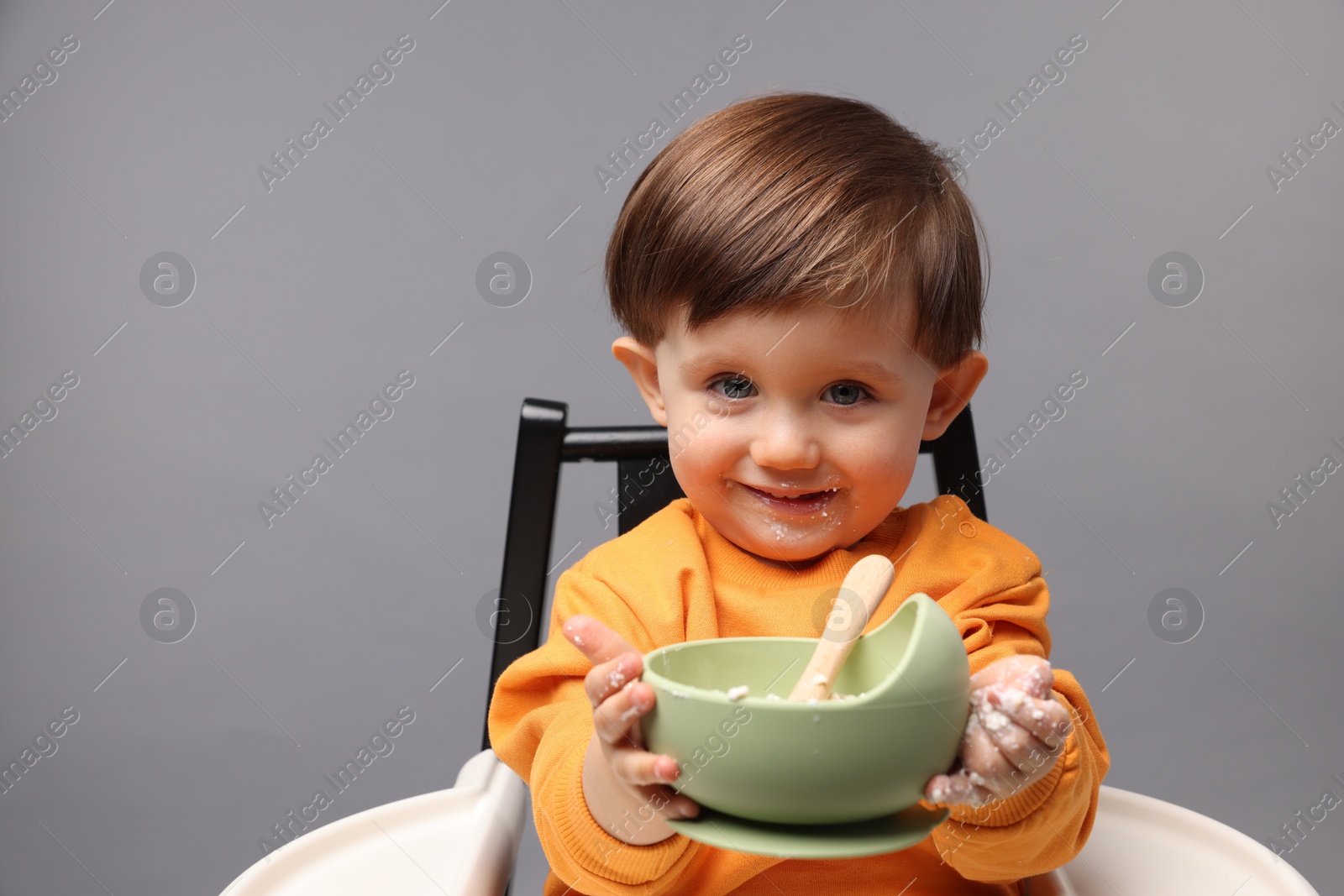 Photo of Cute little kid eating healthy baby food from bowl in high chair on light grey background