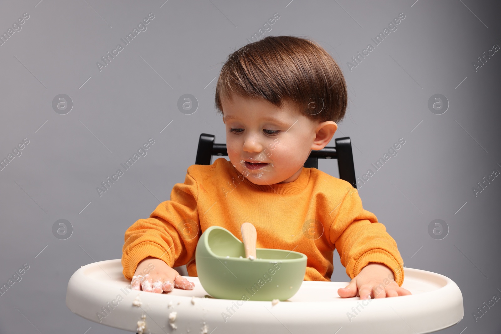 Photo of Cute little kid eating healthy baby food from bowl in high chair on light grey background