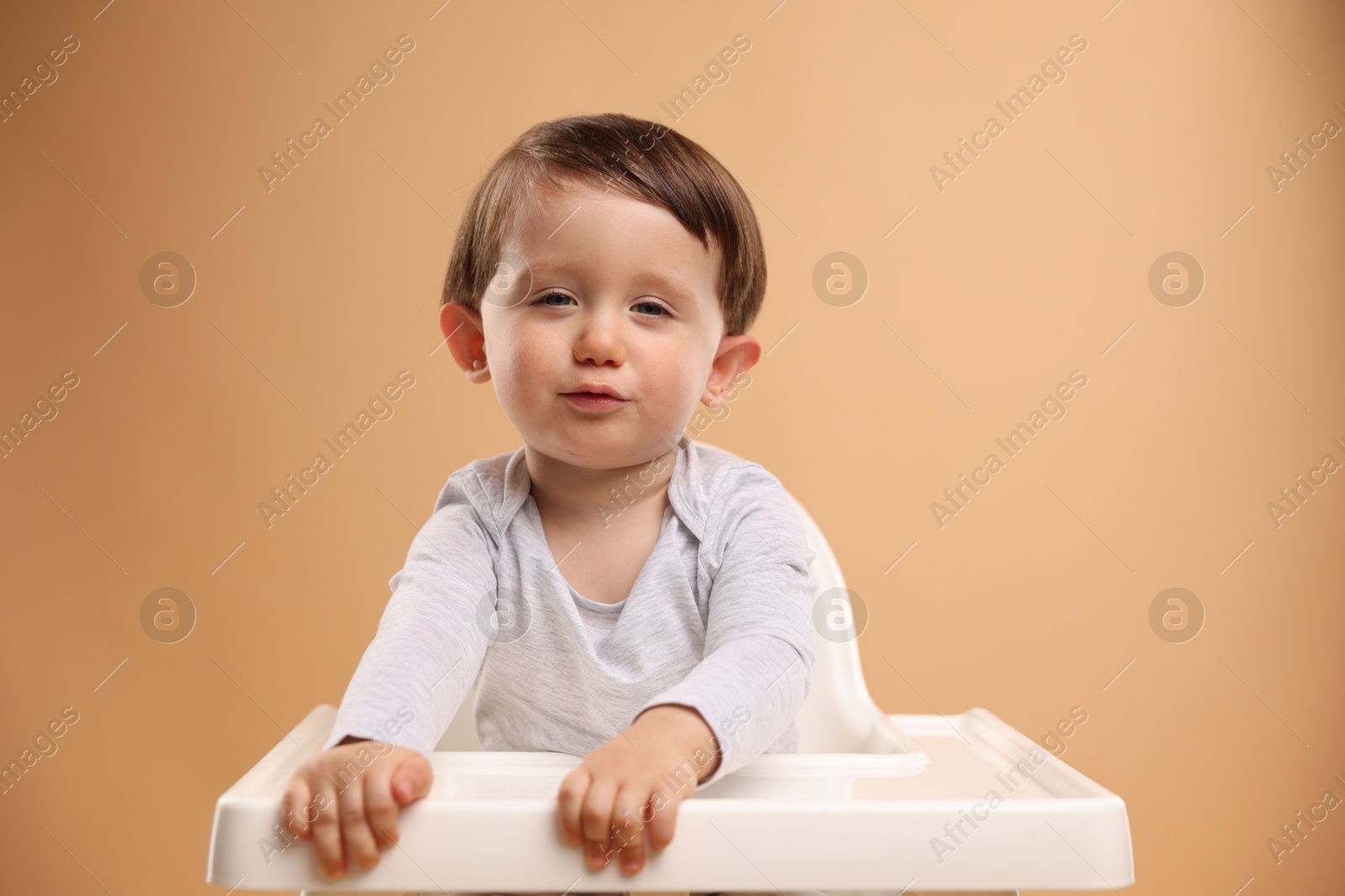 Photo of Cute little kid sitting in high chair on beige background