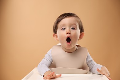 Photo of Cute little kid sitting in high chair on beige background