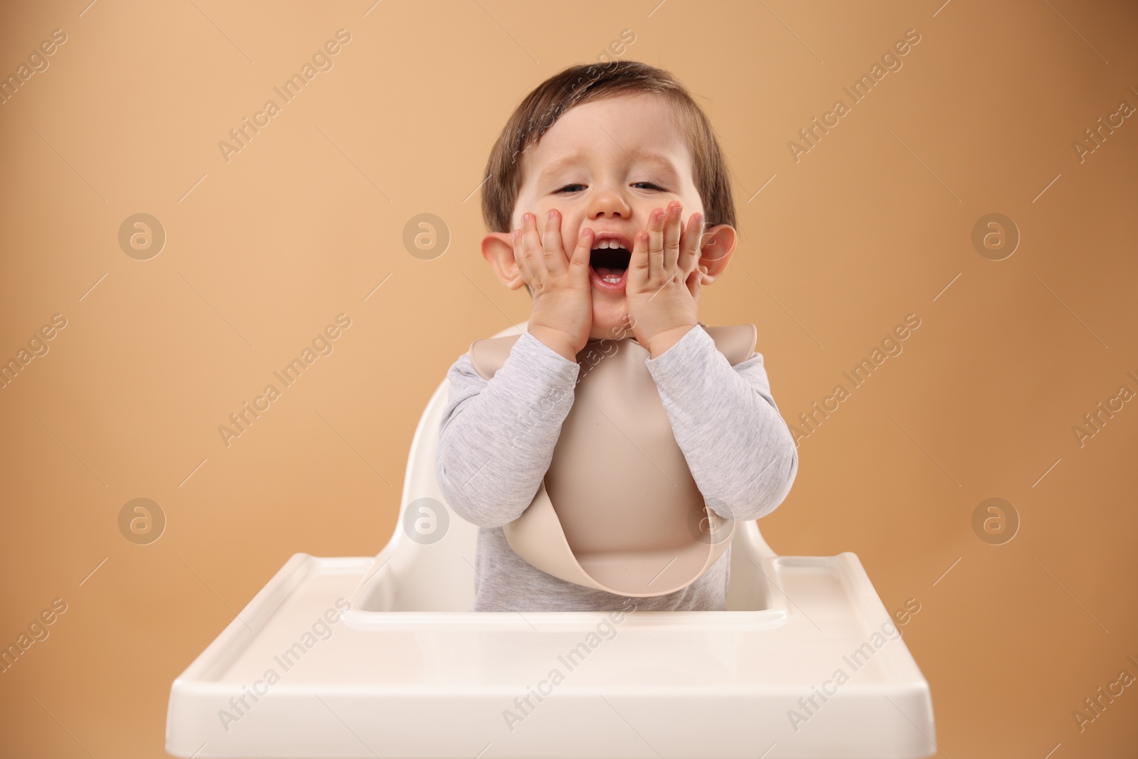 Photo of Cute little kid sitting in high chair on beige background