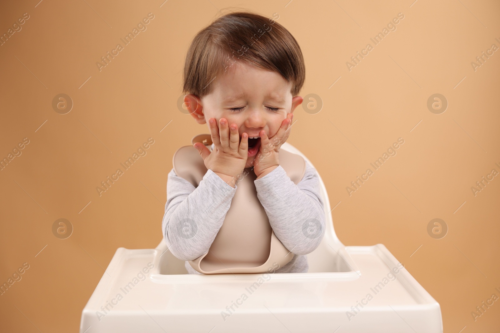 Photo of Cute little kid sitting in high chair on beige background