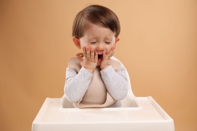 Photo of Cute little kid sitting in high chair on beige background