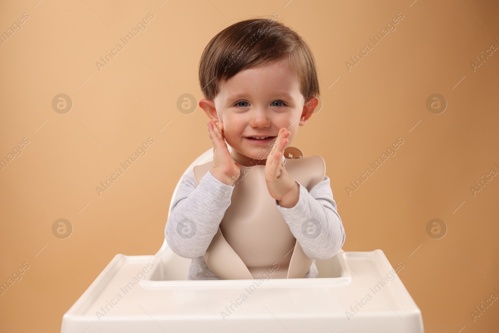 Photo of Cute little kid sitting in high chair on beige background