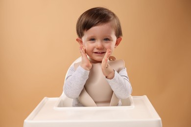 Cute little kid sitting in high chair on beige background