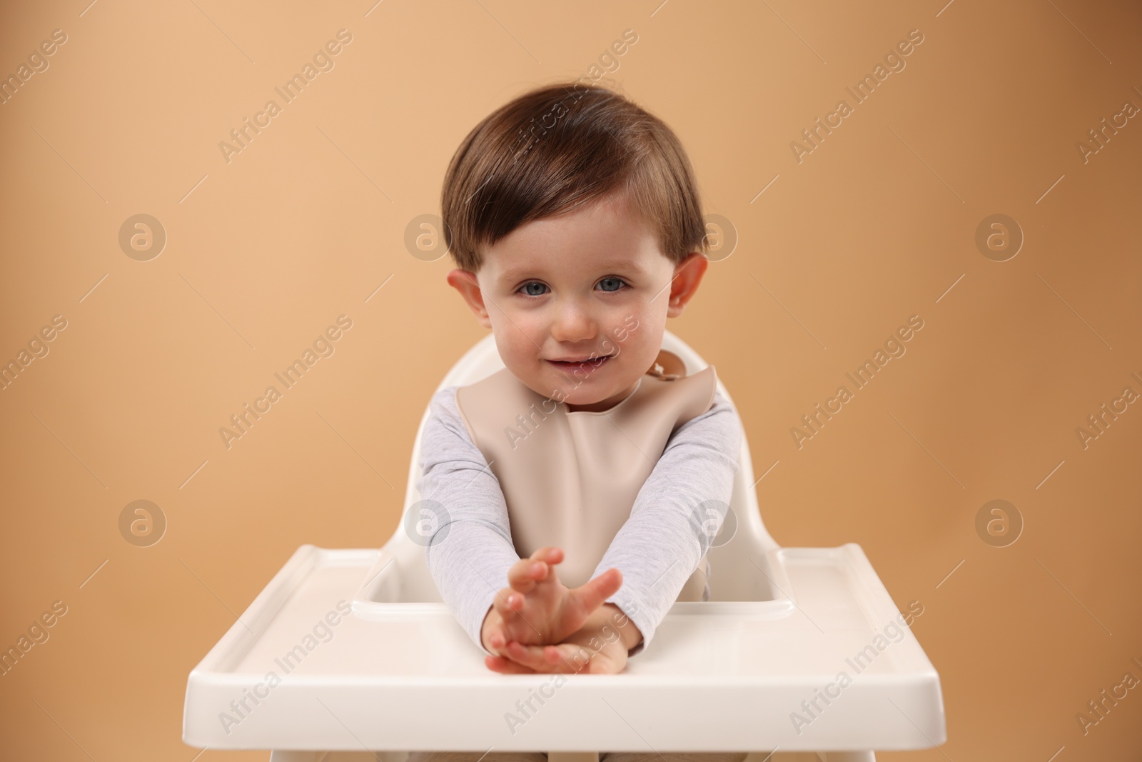 Photo of Cute little kid sitting in high chair on beige background