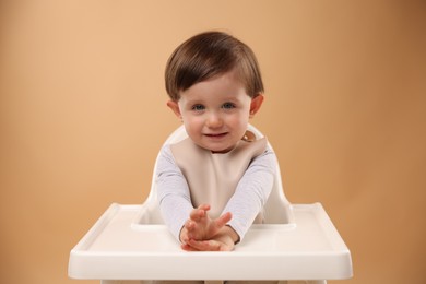 Photo of Cute little kid sitting in high chair on beige background