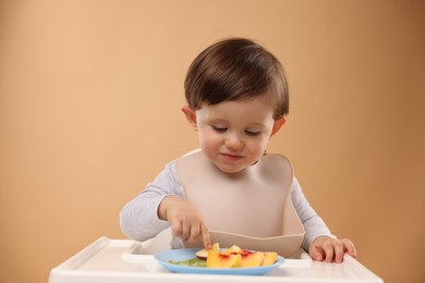 Photo of Healthy baby food. Cute little kid eating fruits in high chair on beige background