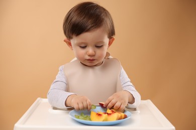 Photo of Healthy baby food. Cute little kid eating fruits in high chair on beige background